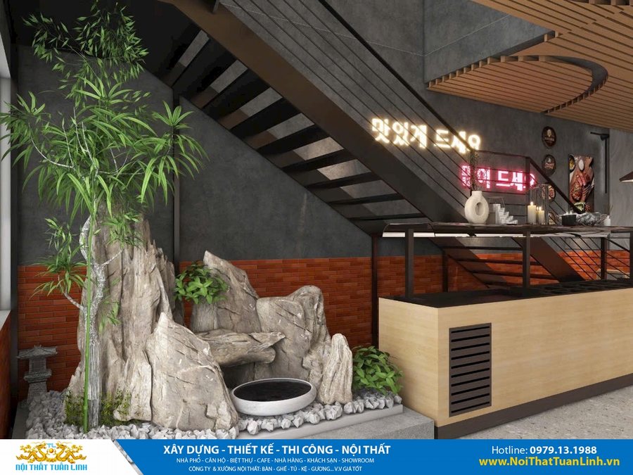 Góc tiểu cảnh dưới cầu thang trong nhà hàng, với đá tự nhiên, cây trúc, hồ nước nhỏ, đèn LED chữ Hàn, tường bê tông kết hợp gạch đỏ, mang phong cách Hàn Quốc hiện đại kết hợp thiên nhiên.